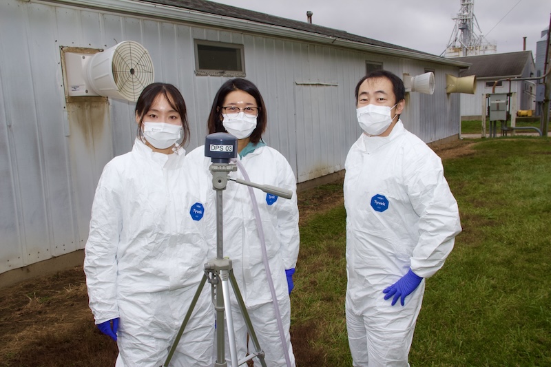 Subin Han, Nara Shin and Jae Hong Park and their air sampler stand outside of a Purdue swine farrowing room.