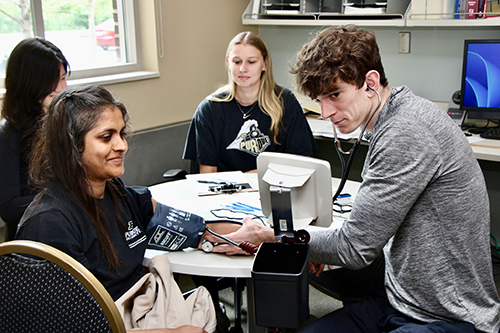 A student takes the blood pressure of someone receiving a fitness assessment.