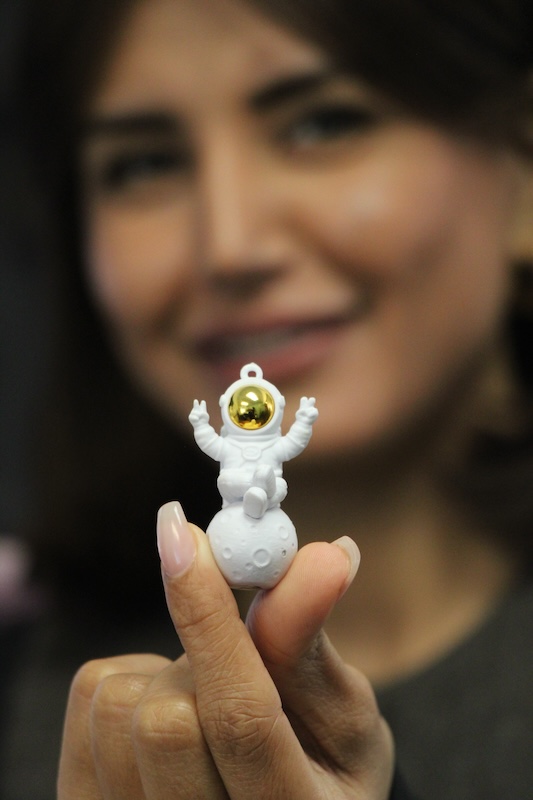 Roya Alavipour holds a toy astronaut sitting on a small moon.