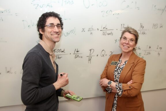 Benji Milanowski and Professor Ann Loomis stand in front of a white board with math equations on it.