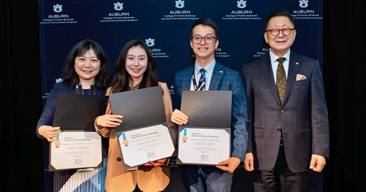Three people stand with certificates next to an award presenter.