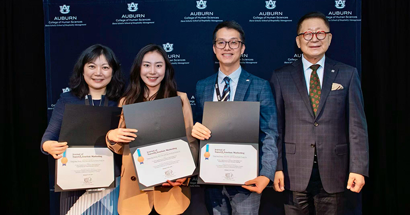 Three people stand with certificates next to an award presenter.