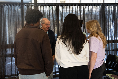 Students stand in a group, talking to an older gentleman.