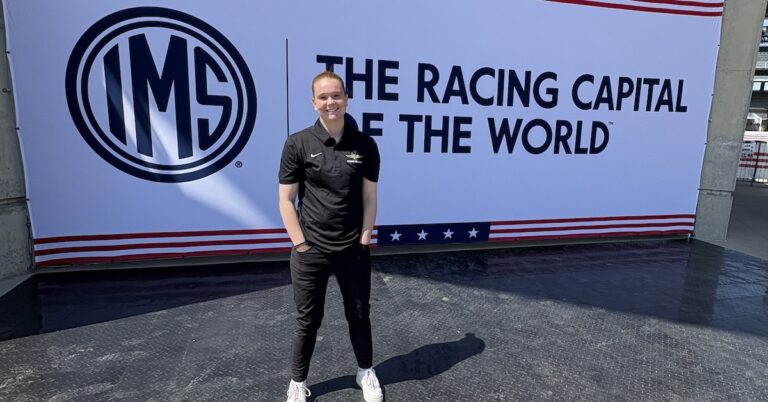 Molly Wendell stands in front of a sign at the Indiana Motor Speedway.