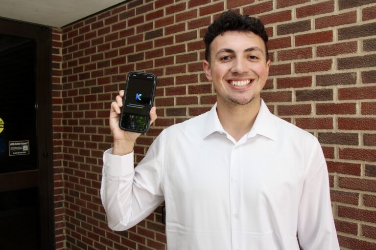 Tyson Magee shows his new app Kintec AI in front of a brick wall.