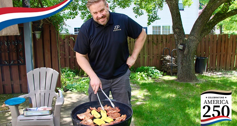 Shawn Bucher poses behind his barbecue pit while holding tongs.