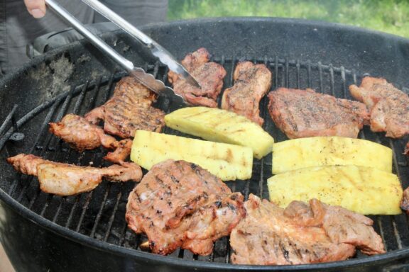 Pork and pineapple is being grilled with tongs moving the items around.