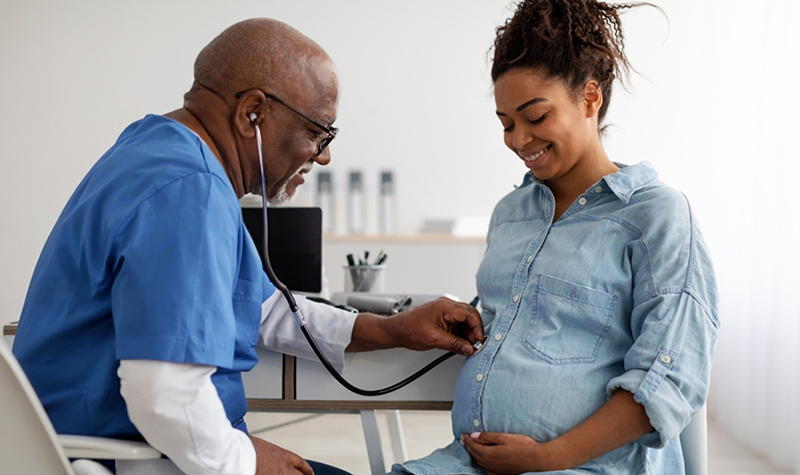 A nurse listens to a pregnant woman's stomach with a stethoscope.