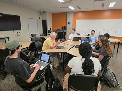 Dean Aaron Bowman talks to a group of students sitting around a table.