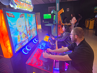 Jonathan Shannahan plays an arcade game with a student.