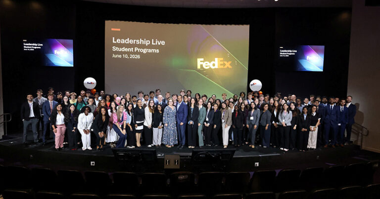 A large group of FedEx interns stand on a stage in an auditorium.