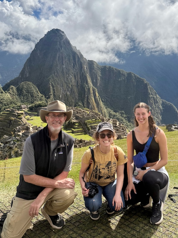 Jonathon Day, Sarah Renkert and Taylor Cawood crouch down for a photo in front of Machu Picchu.