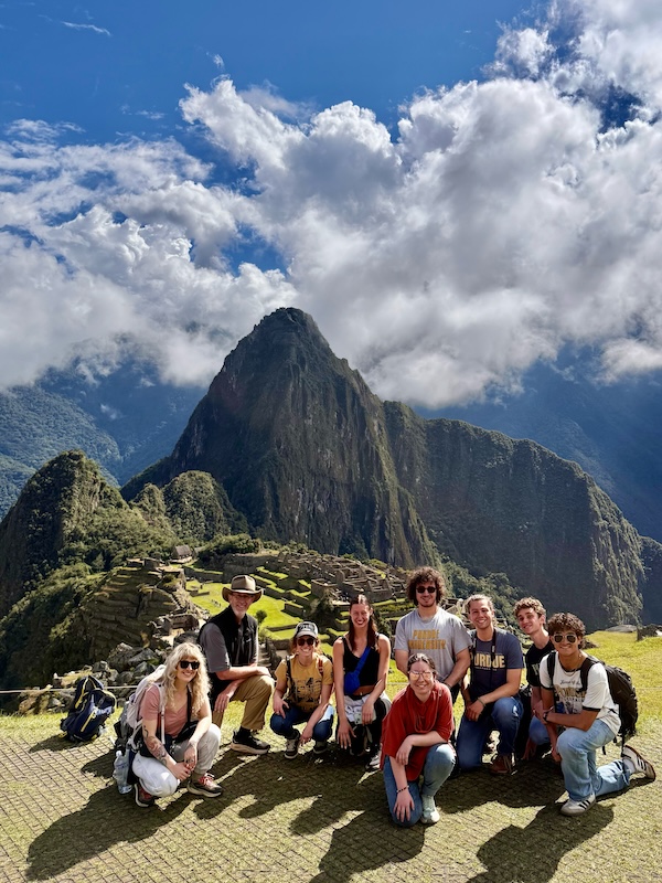 Jonathon Day and students crouch down for a photo in front of Machu Picchu