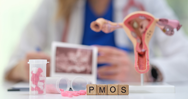 A stock image of a uterus model with letter tiles in front of it that says "PMOS."