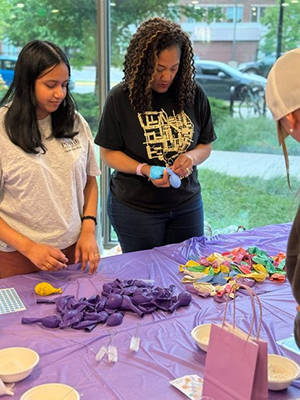 Solari Williams holds a balloon that she is filling, standing in a group with students.