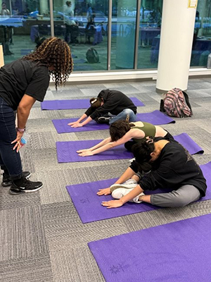 Students pose on yoga mats while Solari Williams coaches them from the front of the space.