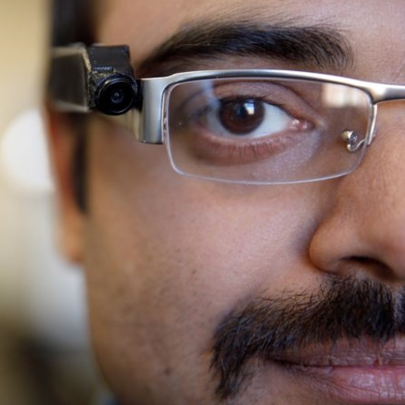 A closeup image of a man wearing a tiny camera on his eye glasses frame.
