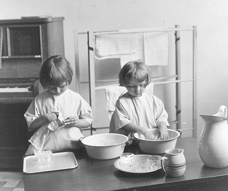 Two young girls pretend to wash dishes in the lab school.