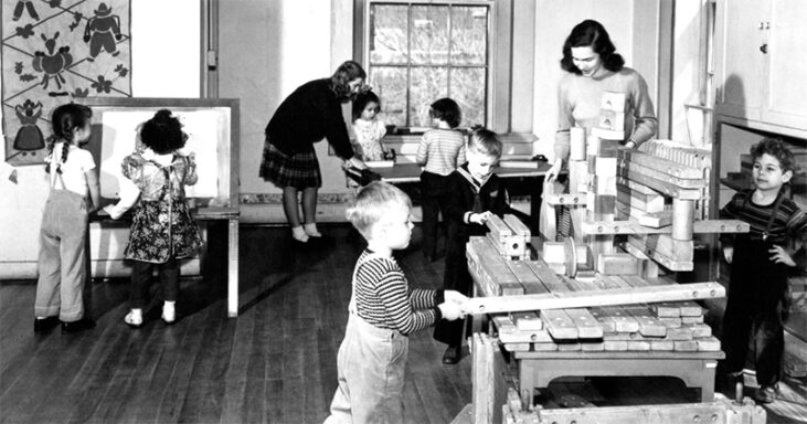 A black-and-white photo of children playing with blocks and others making art in the background.