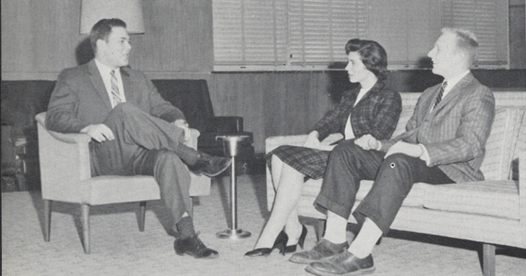 A black-and-white photo of students sitting in a lounge talking.