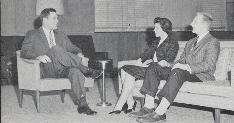 A black-and-white photo of students sitting in a lounge talking.