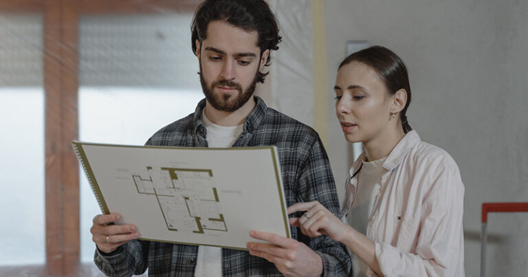 A couple looks at a house plan with one appearing to be correcting the other; both look unhappy.