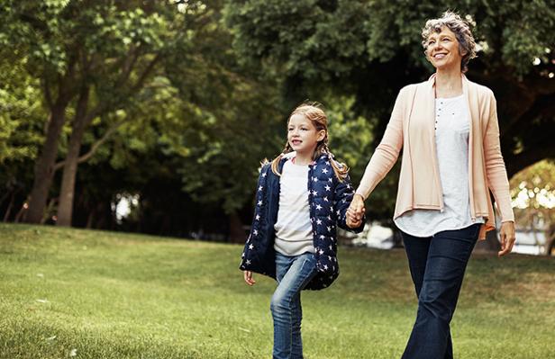 A woman and child hold hands while walking in a park.