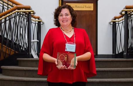 Kathleen Abrahamson stands holding an engraved glass award