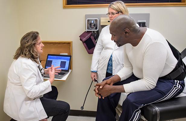 Two nurses speak with an adult patient in an examination room.