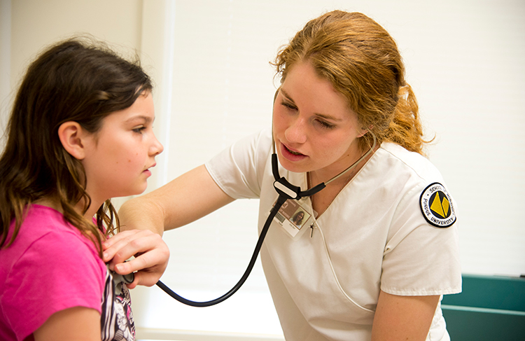 A nurse holds a stethoscope to a young girl’s chest.
