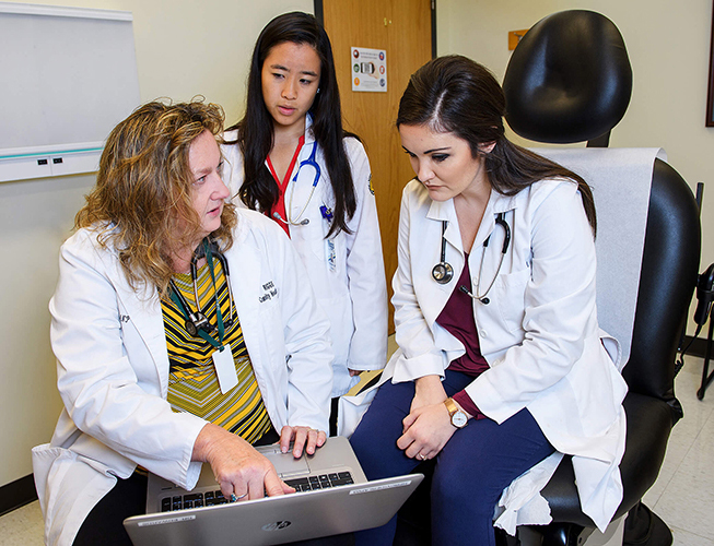 Nancy Edwards talks to nursing students while holding a laptop