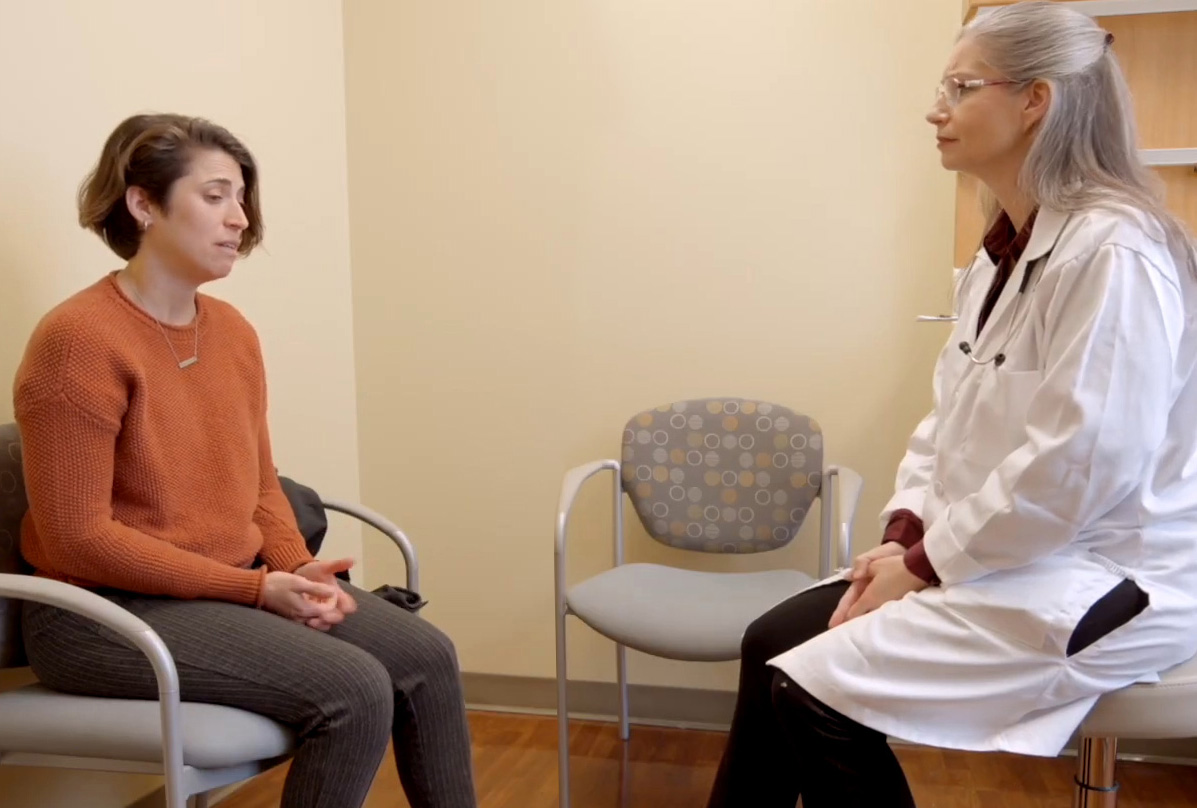 A screenshot of a video of a woman in a medical room speaking to a nurse practitioner