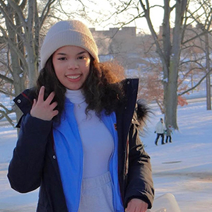 Sarah Lopez wearing a hat and winter coat walking through a park on a snowy day