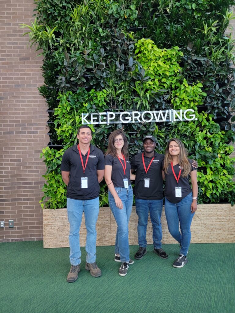 Four grad students standing in front of a plant wall with the words 'Keep Growing'