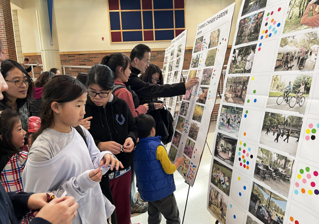 A group of young and old looking at concepts on posterboard and placing stickers on their favorites.
