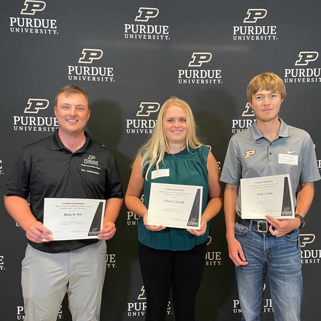 Brody Piel, Emma Seward, and Jacob Tower standing in front of the Purdue backdrop holding their certificates.