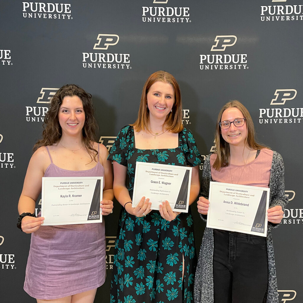 Kayla Kramer, Grace Wagner, and Anna Hildebrand stand in front of the Purdue backdrop holding their certificates.