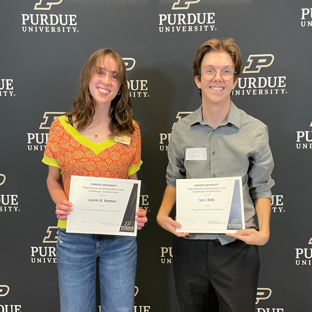Lauren Harmon and Ian Kelly standing in front of the Purdue backdrop holding their certificates.