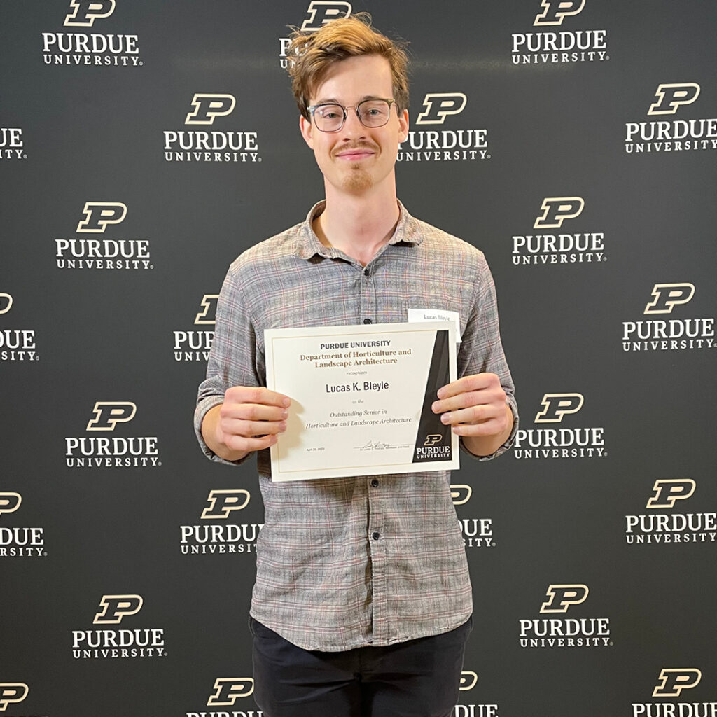 Lucas Bleyle stands in front of the Purdue backdrop with his certificate.