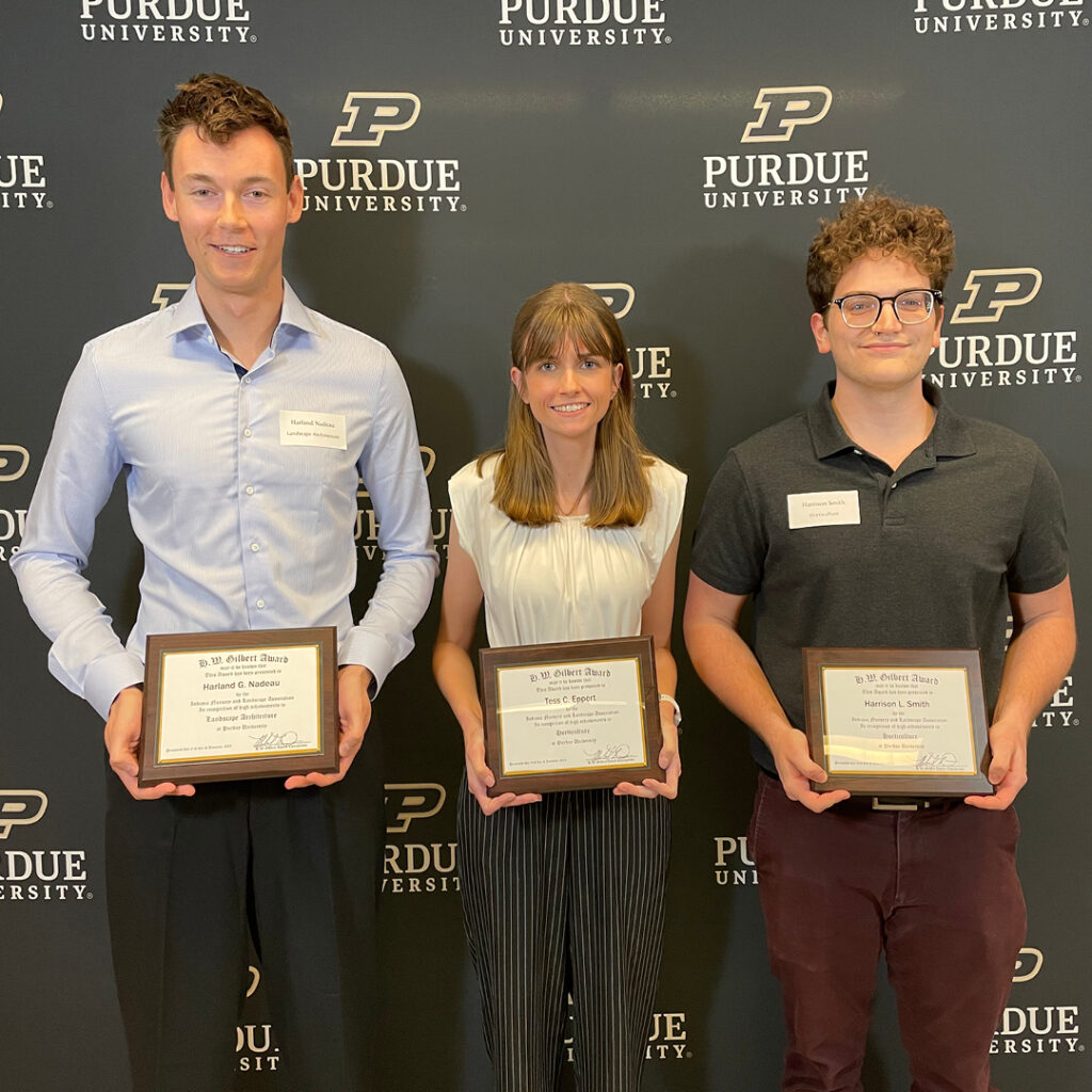 Harland Nadeau, Tess Eppert, and Harrison Smith standing in front of the Purdue backdrop holding their plaques.