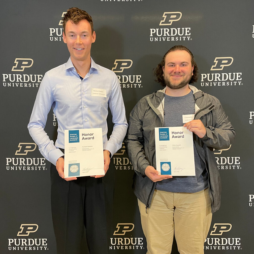 Harland Nadeau and Chris Curnell standing in front of the Purdue backdrop holding their certificates.
