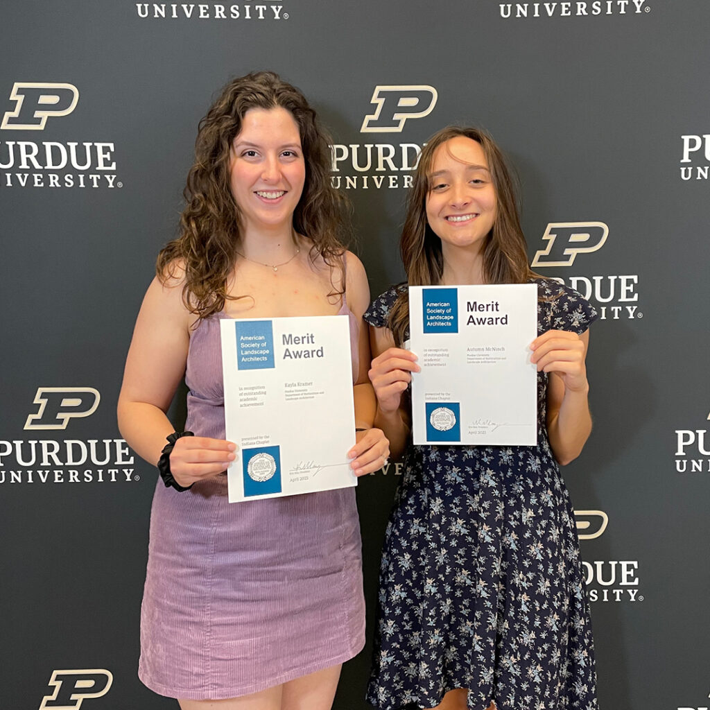 Kayla Kramer and Autumn McNinch standing in front of the Purdue backdrop holding their certificates.