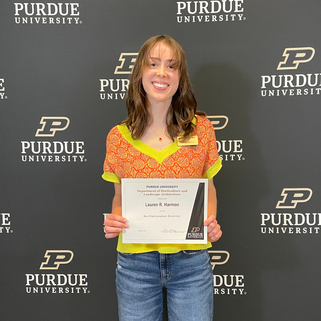 Lauren Harmon standing in front of the Purdue backdrop holding her certificate.