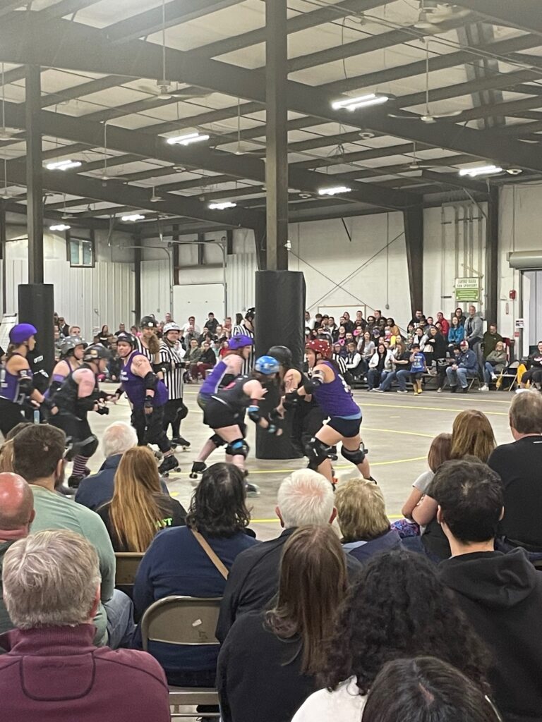 Roller derby action while the crowd watches on.
