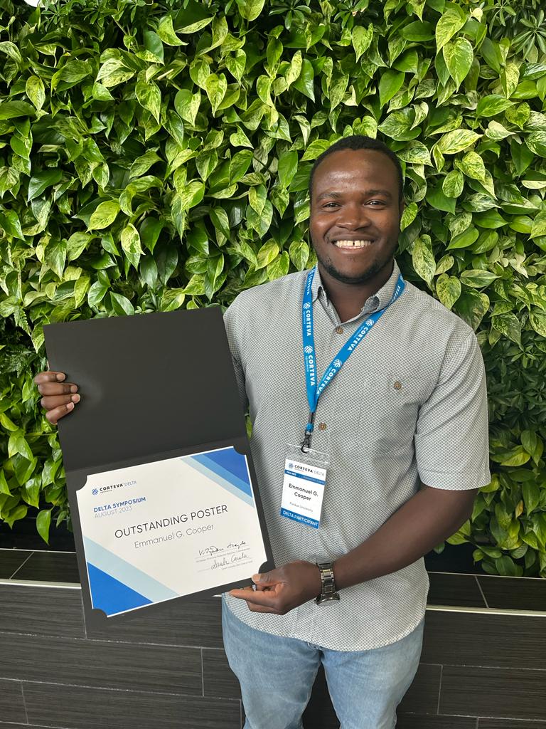 Emmanuel Cooper standing in front of the green wall holding his outstanding poster presentation award.