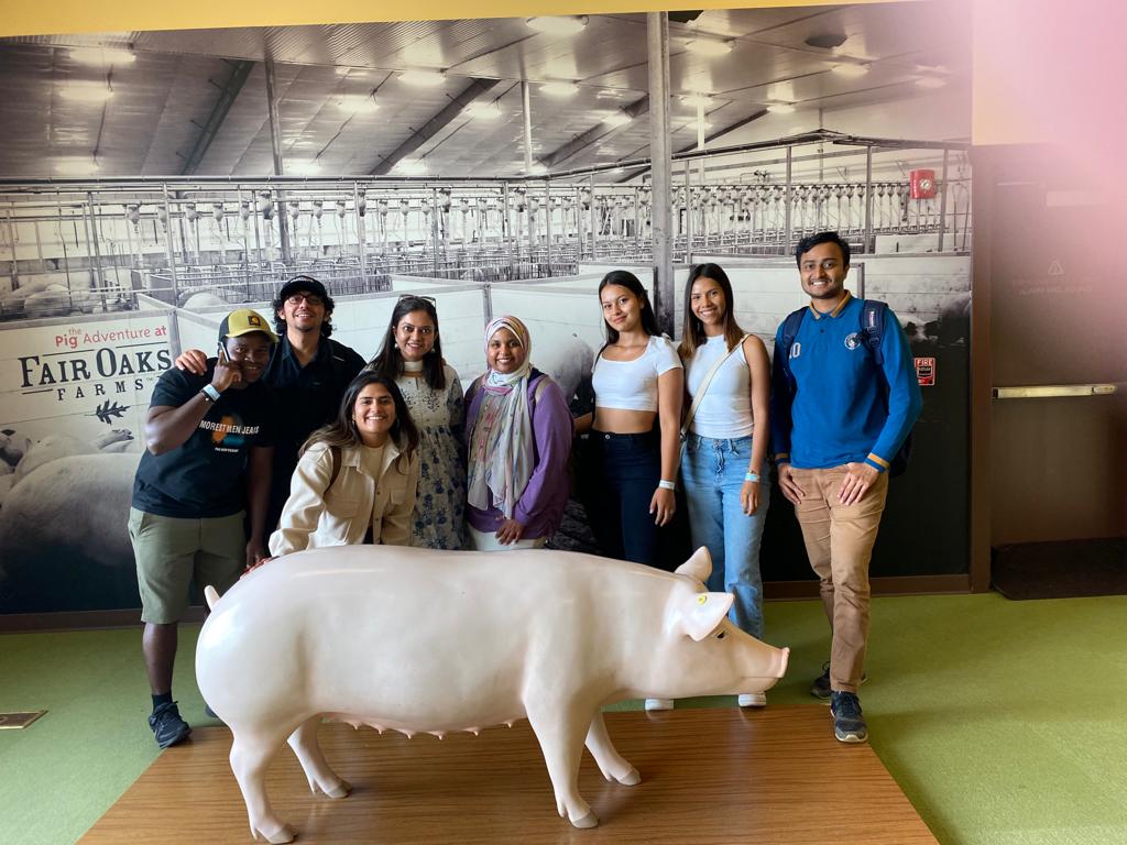 Photo of grad students standing behind small pig statue