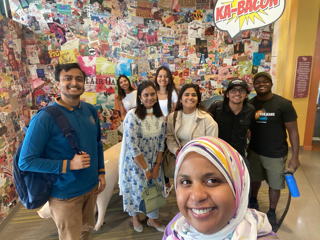 Selfie of grad students standing near a collage wall art.