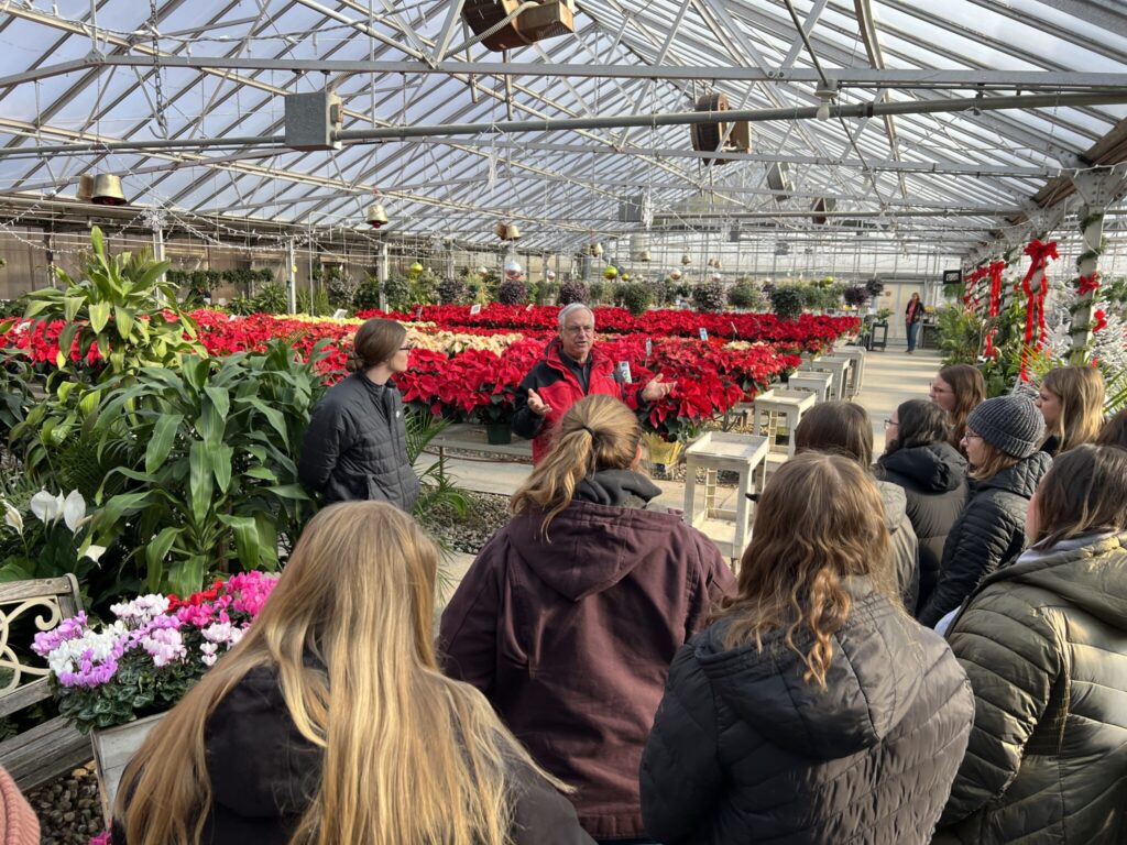 Students listening to a representative of Bennett's Greenhouse surrounded with lots of red poinsettias.