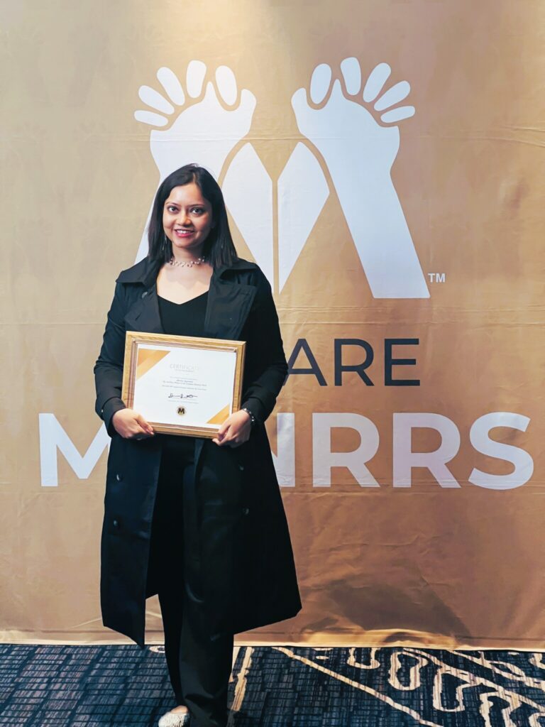Shivika Aggrawal standing in front a MANRRS banner holding a certificate.