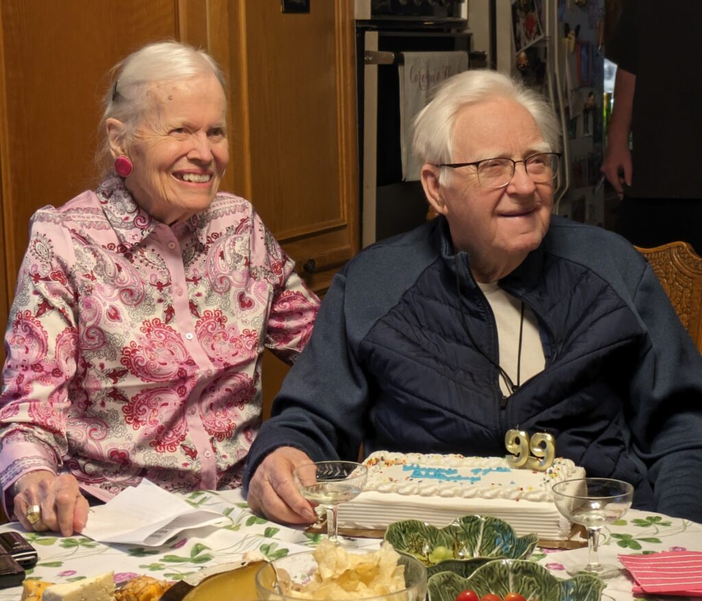 Homer Erickson and wife sitting with birthday cake with candles saying 99.